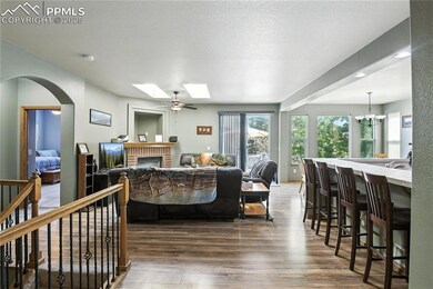 Living room with dark wood finished floors, a skylight, a brick fireplace, a chandelier, and arched walkways