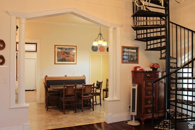 Dining area featuring ornate columns, stairway, wood finished floors, and crown molding