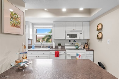 Kitchen with dark countertops, white appliances, white cabinets, and recessed lighting