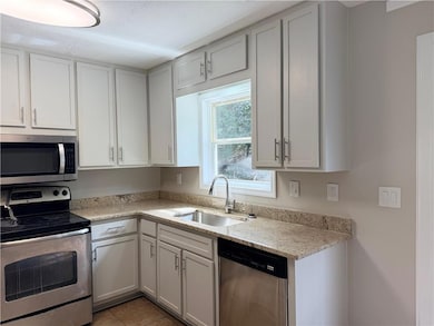 Kitchen featuring appliances with stainless steel finishes, light stone counters, white cabinetry, and light tile patterned flooring
