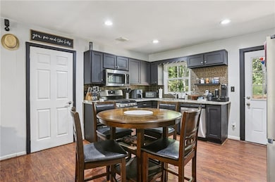 Kitchen with tasteful backsplash, dark wood finished floors, stainless steel appliances, recessed lighting, and light stone countertops