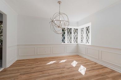 Unfurnished dining area with ornamental molding, a chandelier, a wainscoted wall, light wood-style flooring, and a decorative wall