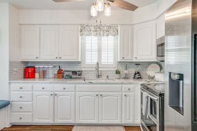 Kitchen with stainless steel appliances, light stone counters, white cabinets, and decorative backsplash