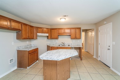 Kitchen featuring under cabinet range hood, brown cabinets, a kitchen island, and light tile patterned flooring
