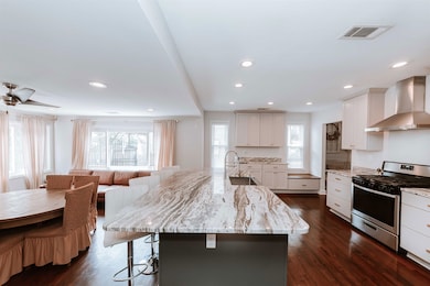 Kitchen with stainless steel gas range, wall chimney range hood, a sink, a kitchen bar, and light stone countertops