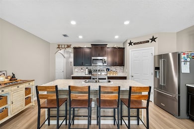 Kitchen featuring appliances with stainless steel finishes, a kitchen bar, backsplash, a kitchen island with sink, and dark brown cabinets