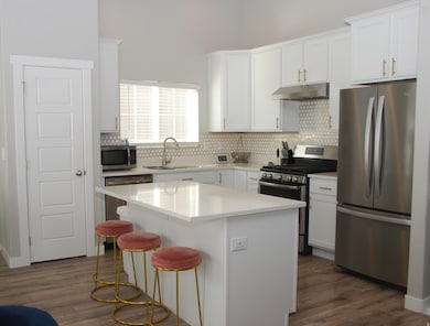 Kitchen featuring appliances with stainless steel finishes, white cabinets, decorative backsplash, and a kitchen island