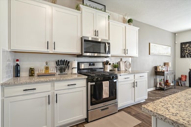 Kitchen featuring appliances with stainless steel finishes, dark wood-style flooring, white cabinets, backsplash, and a textured ceiling