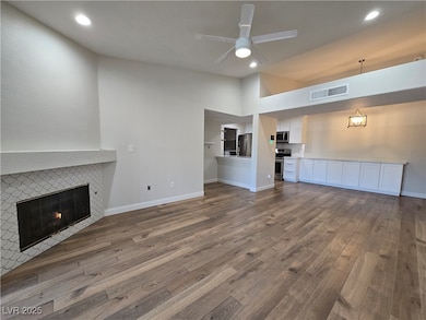 Unfurnished living room with dark wood finished floors, a tiled fireplace, recessed lighting, ceiling fan, and vaulted ceiling