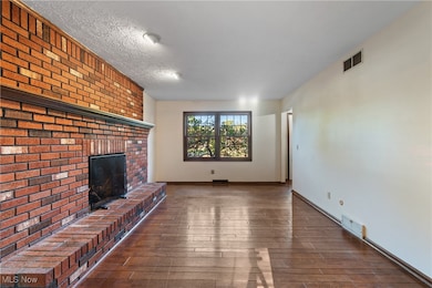 Unfurnished family room with a brick fireplace, hardwood / wood floors, and a textured ceiling