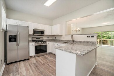 Kitchen featuring stainless steel appliances, a sink, a peninsula, a chandelier, and light wood-style floors