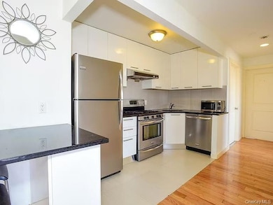 Kitchen featuring stainless steel appliances, white cabinetry, under cabinet range hood, tasteful backsplash, and modern cabinets