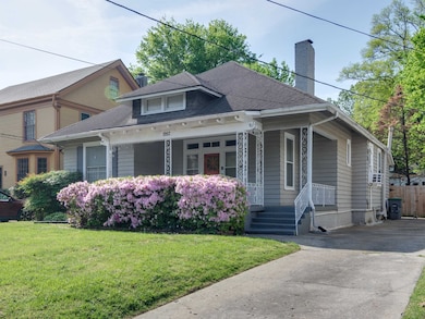 View of front of home with covered porch, a chimney, a front lawn, and roof with shingles
