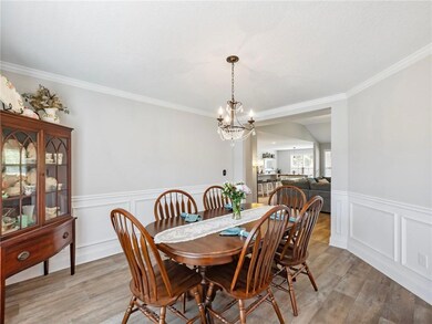Dining space with a chandelier, light wood-style flooring, crown molding, a wainscoted wall, and a decorative wall