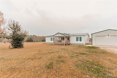 Manufactured / mobile home with a front lawn, an outdoor structure, a metal roof, a garage, and covered porch