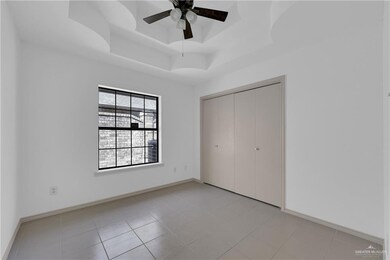 Unfurnished bedroom featuring ceiling fan, light tile patterned flooring, baseboards, a closet, and a tray ceiling