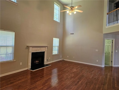 Unfurnished living room with a high ceiling, a ceiling fan, wood finished floors, and a fireplace with raised hearth