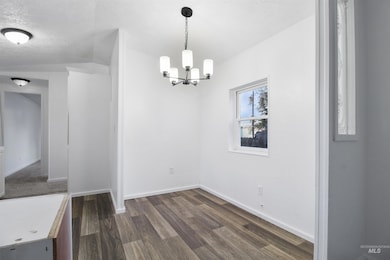 Unfurnished dining area featuring dark wood-style floors, a textured ceiling, and a chandelier