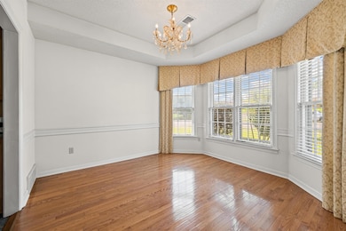 Empty room featuring a chandelier, wood finished floors, a raised ceiling, and a textured ceiling