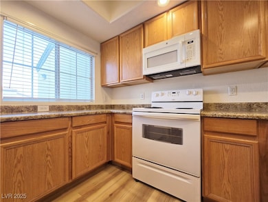 Kitchen with white appliances, brown cabinets, and light wood-style floors