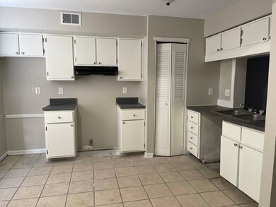 Kitchen featuring under cabinet range hood, dark countertops, white cabinets, and light tile patterned floors
