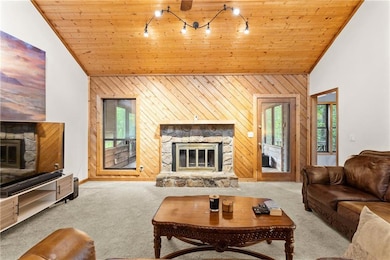 Living room featuring a stone fireplace, vaulted ceiling, carpet, wooden walls, and wooden ceiling