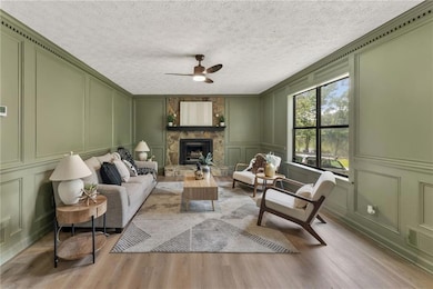 Living room with a decorative wall, light wood finished floors, ceiling fan, and a fireplace