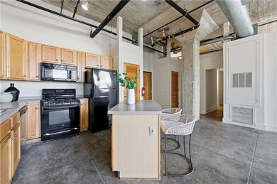 Kitchen with light brown cabinetry, black appliances, a kitchen island, a breakfast bar area, and a towering ceiling