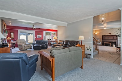 Carpeted living room with a textured ceiling, a chandelier, wallpapered walls, a ceiling fan, and crown molding