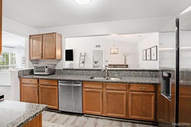 Kitchen with brown cabinets, appliances with stainless steel finishes, dark stone countertops, light wood finished floors, and hanging light fixtures