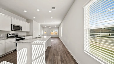 Kitchen with stainless steel appliances, white cabinetry, an island with sink, recessed lighting, and light stone countertops