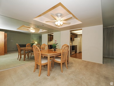 Dining room with a tray ceiling, light carpet, and ceiling fan