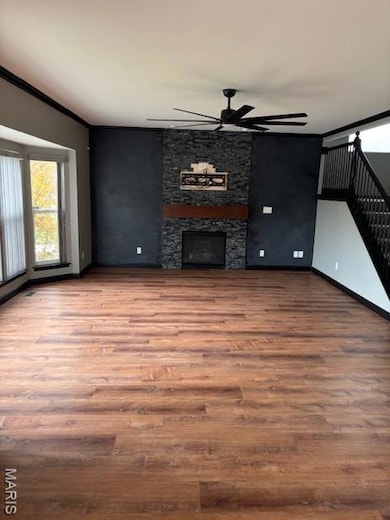 Unfurnished living room with stairway, a fireplace, wood finished floors, a ceiling fan, and ornamental molding