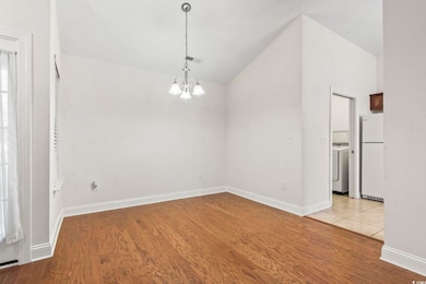Unfurnished dining area with vaulted ceiling, a chandelier, wood finished floors, and washer / clothes dryer