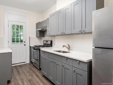 Kitchen featuring gray cabinetry, appliances with stainless steel finishes, dark wood-style floors, under cabinet range hood, and light stone countertops