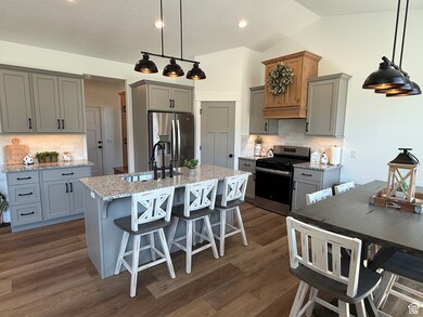 Kitchen featuring stainless steel appliances, a center island with sink, decorative backsplash, gray cabinets, and vaulted ceiling