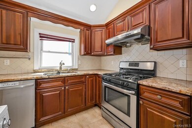 Kitchen with appliances with stainless steel finishes, under cabinet range hood, light stone countertops, backsplash, and light tile patterned flooring
