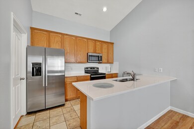 Kitchen with stainless steel appliances, backsplash, a peninsula, light stone counters, and brown cabinets