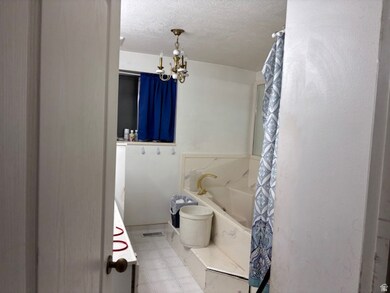 Full bath featuring a tub with marble appearance, a chandelier, a shower with curtain, a textured ceiling, and tile patterned floors