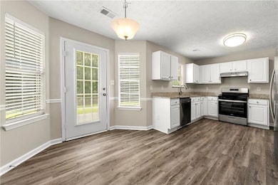 Kitchen with appliances with stainless steel finishes, under cabinet range hood, dark wood-style flooring, white cabinetry, and a textured ceiling