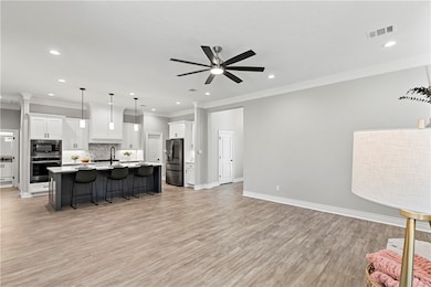 Kitchen featuring a kitchen breakfast bar, ornamental molding, pendant lighting, white cabinets, and light wood-style floors