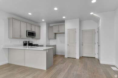 Kitchen featuring appliances with stainless steel finishes, gray cabinets, light wood-style flooring, a peninsula, and baseboards