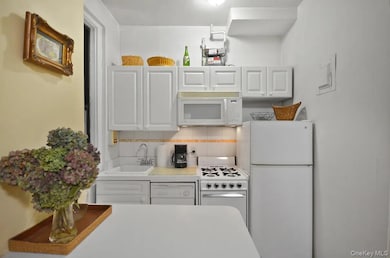 Kitchen with white appliances, white cabinets, light countertops, and decorative backsplash