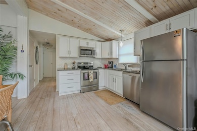 Kitchen featuring appliances with stainless steel finishes, white cabinetry, lofted ceiling, tasteful backsplash, and hanging light fixtures