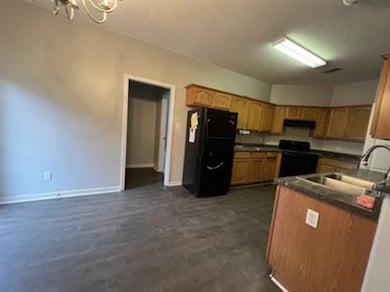 Kitchen featuring freestanding refrigerator, range, dark countertops, brown cabinetry, and a chandelier