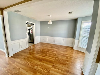 Unfurnished dining area featuring wainscoting, a decorative wall, light wood finished floors, and a textured ceiling