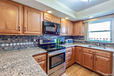 Kitchen featuring stainless steel range with electric cooktop, light stone counters, black microwave, decorative backsplash, and recessed lighting