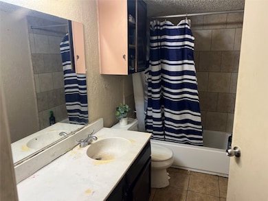 Bathroom featuring a textured wall, vanity, shower / bath combination with curtain, dark tile patterned flooring, and a textured ceiling