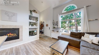 Living room featuring high vaulted ceiling, wood finished floors, a tiled fireplace, and built in features