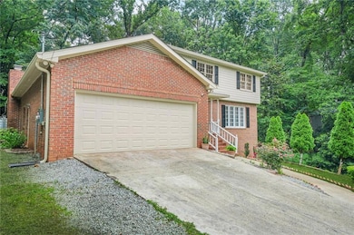 View of front of home featuring a garage, driveway, brick siding, and view of wooded area